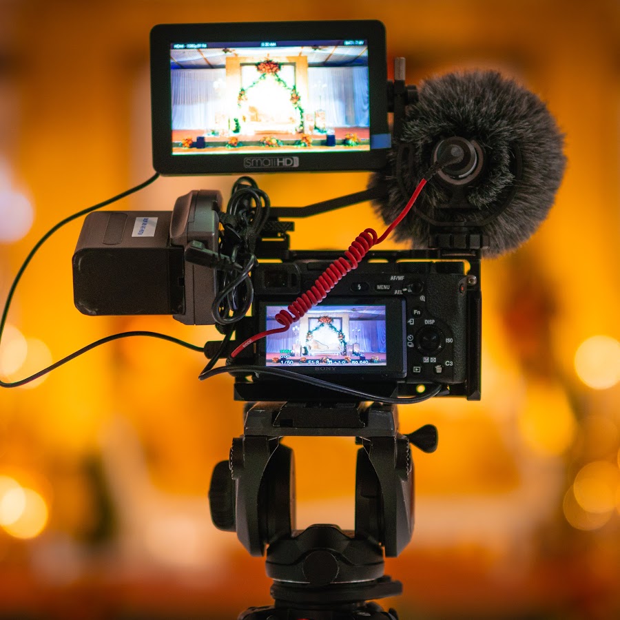 Une caméra vidéo sur un trépied, éclairée par une lumière située derrière elle.